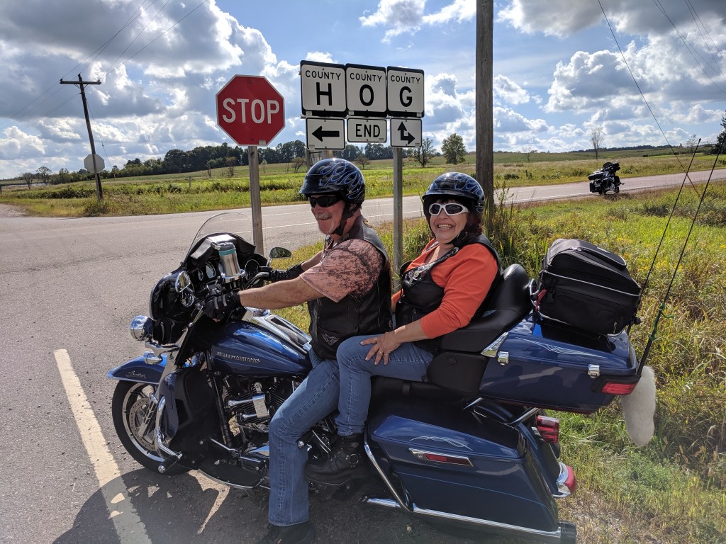 Dan and Linda on Harley near road sign intersection of Hwy H, O, G. in western Wisconsin.